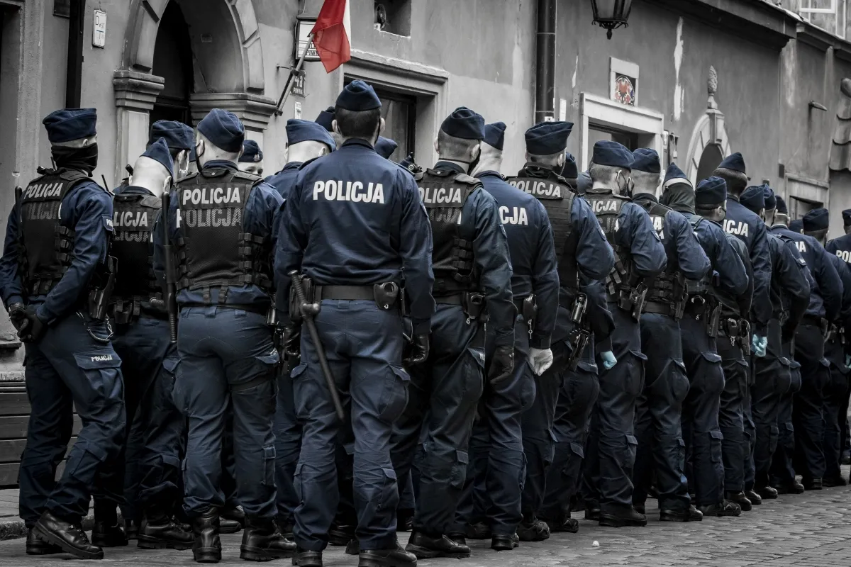 Police line seen from behind beneath a red flag on an old city street